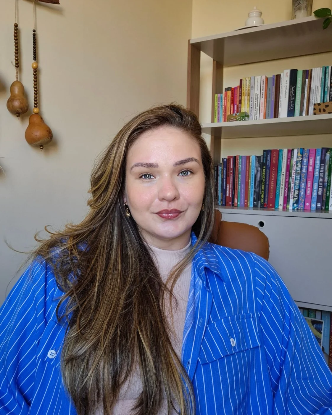 Nathália Braz de camisa azul no consultório, com estante de livros ao fundo